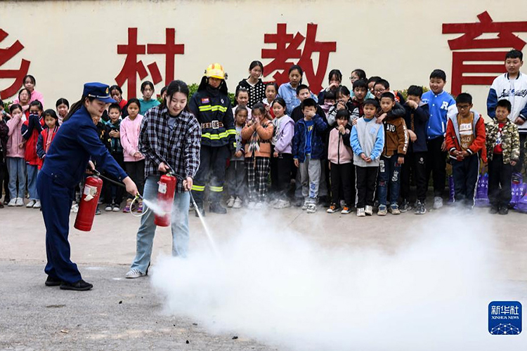 5月10日，在河南省济源市王屋镇大路小学，一名教师在消防员指导下体验用灭火器灭火。（新华社发 苗秋闹摄）.jpg