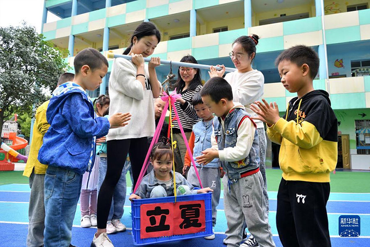5月5日，湖北省襄阳市保康县一家幼儿园的老师用传统方法给孩子称体重。（新华社发 杨韬摄）.jpg